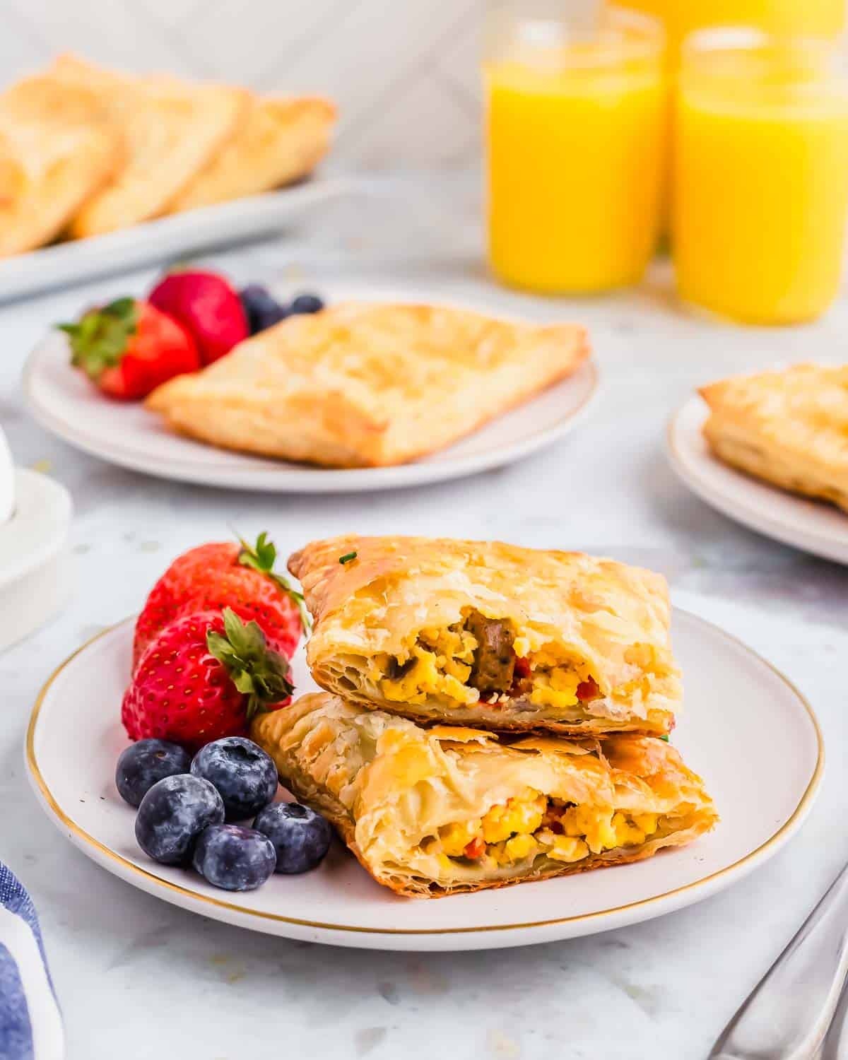 A stack of breakfast pastries on a plate with berries and orange juice.