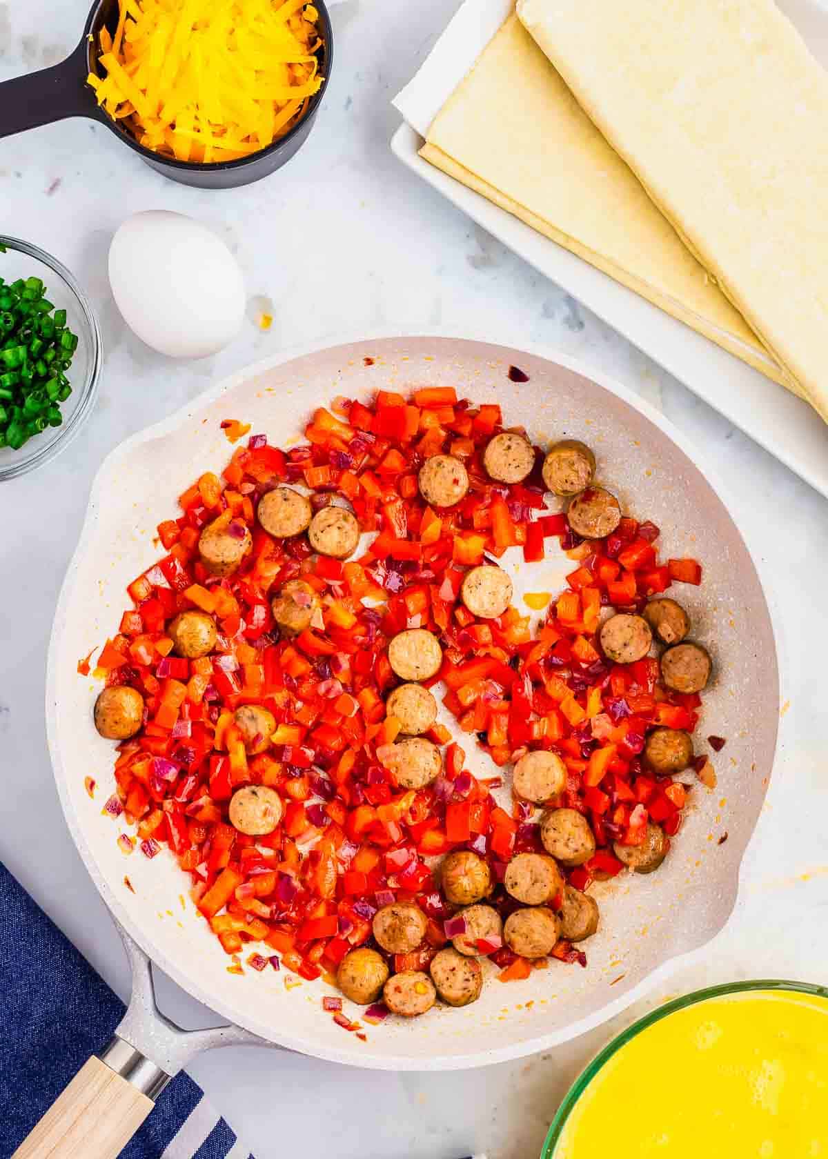 A frying pan with eggs, sausage, peppers and cheese.