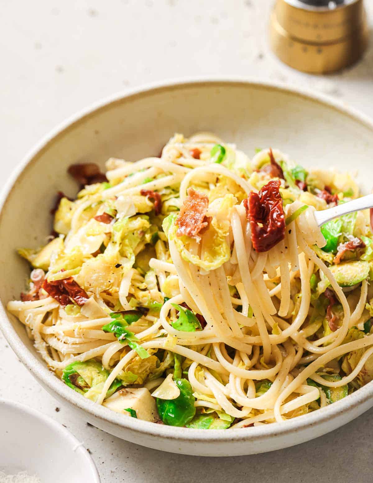 A bowl of pasta with bacon and brussels on a fork.