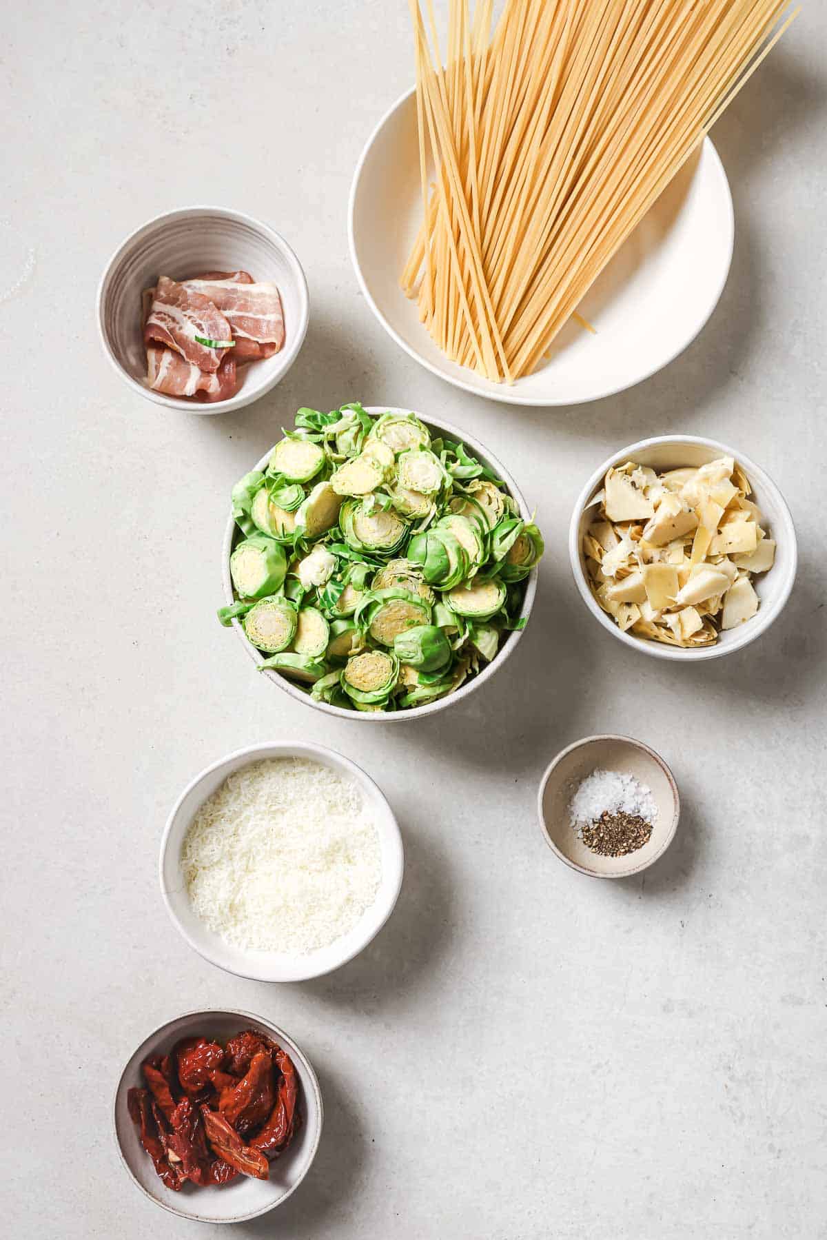 Ingredients for brussels sprouts pasta in bowls on a white surface.