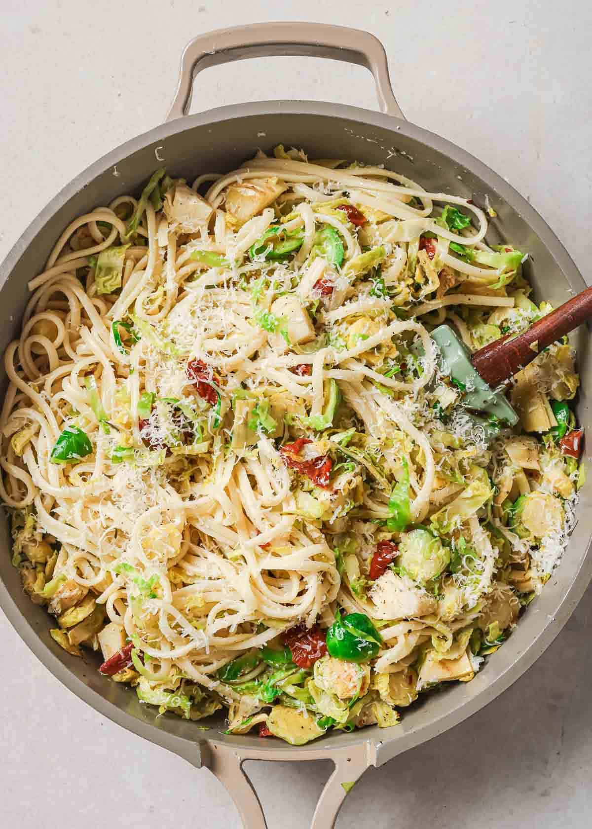 A pan full of pasta with brussels sprouts and grated parmesan cheese.