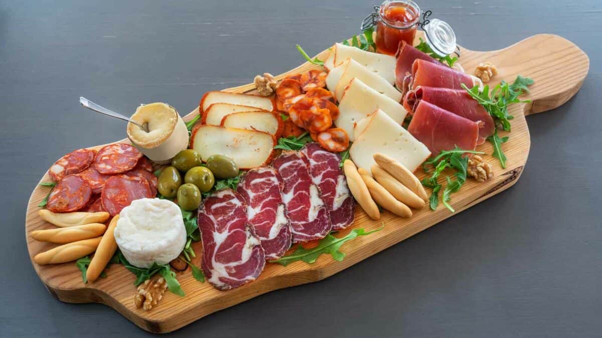 A wooden board with a variety of meats and cheeses.