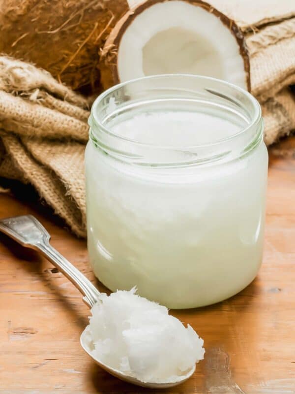 A jar of coconut oil and a spoon on a wooden table.