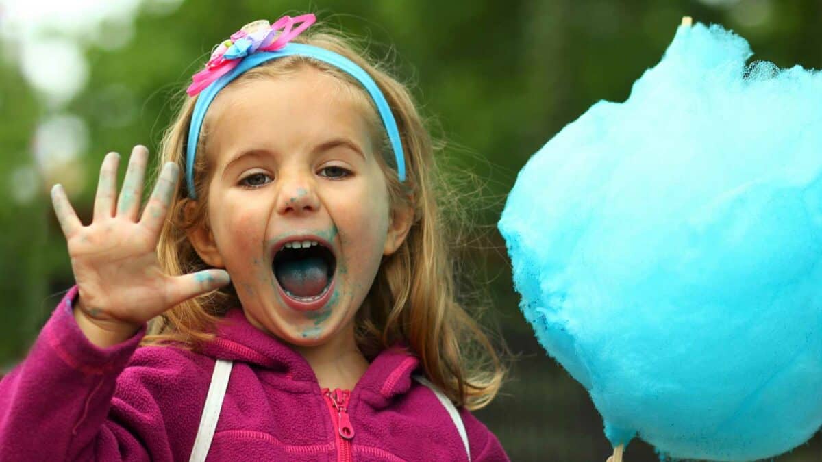 A little girl is holding a blue cotton candy.