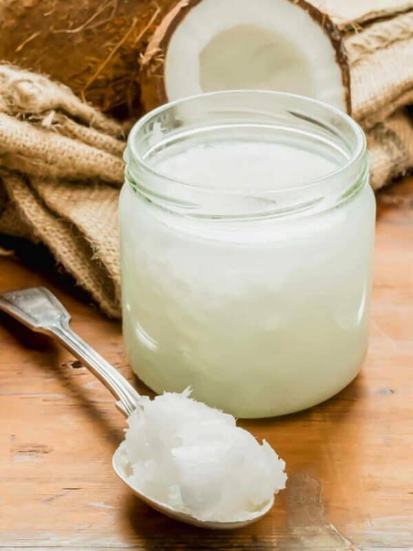 A jar of coconut oil and a spoon on a wooden table.