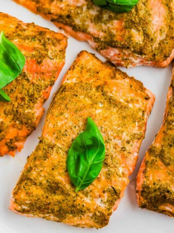 Four salmon fillets with basil leaves on a plate.