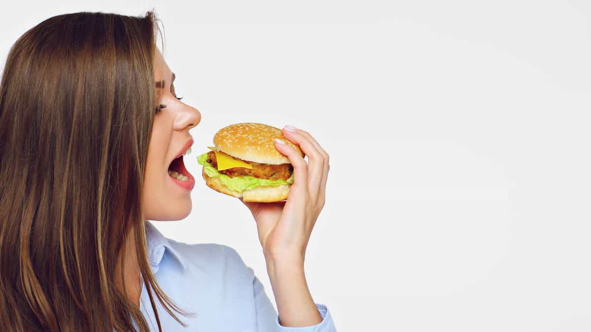 A woman is eating a hamburger with her mouth open.