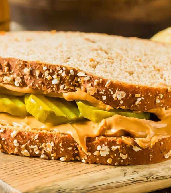 A sandwich with peanut butter and pickles on a wooden cutting board.