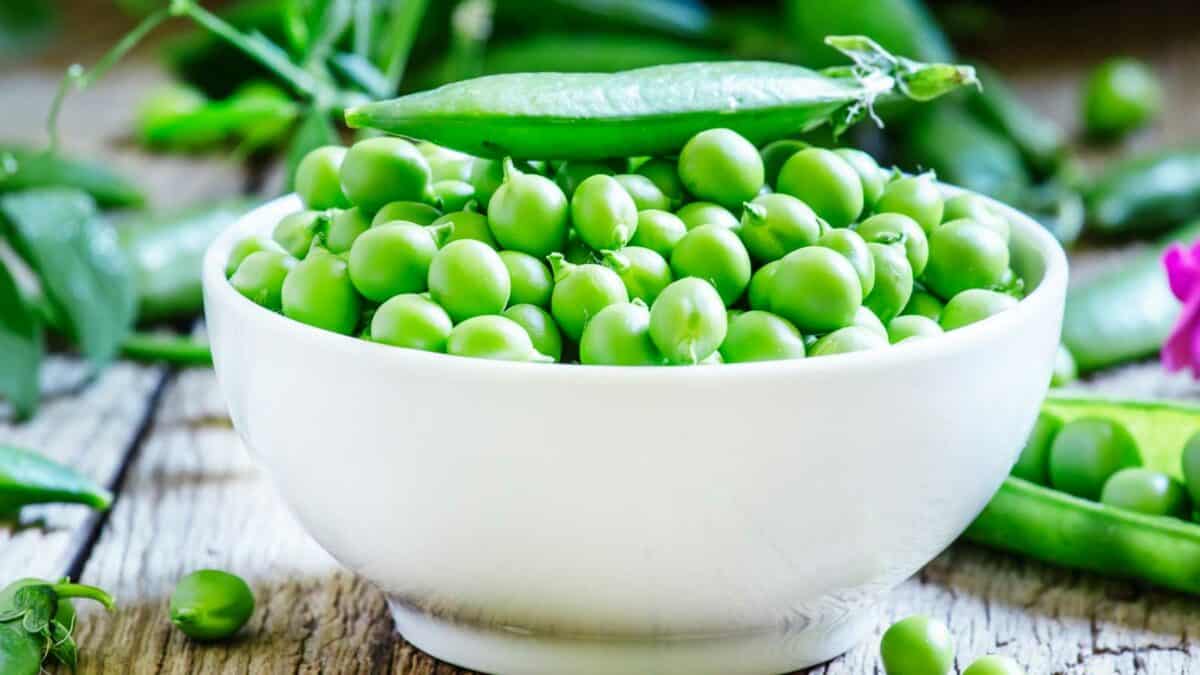 Peas in a white bowl on a wooden table.