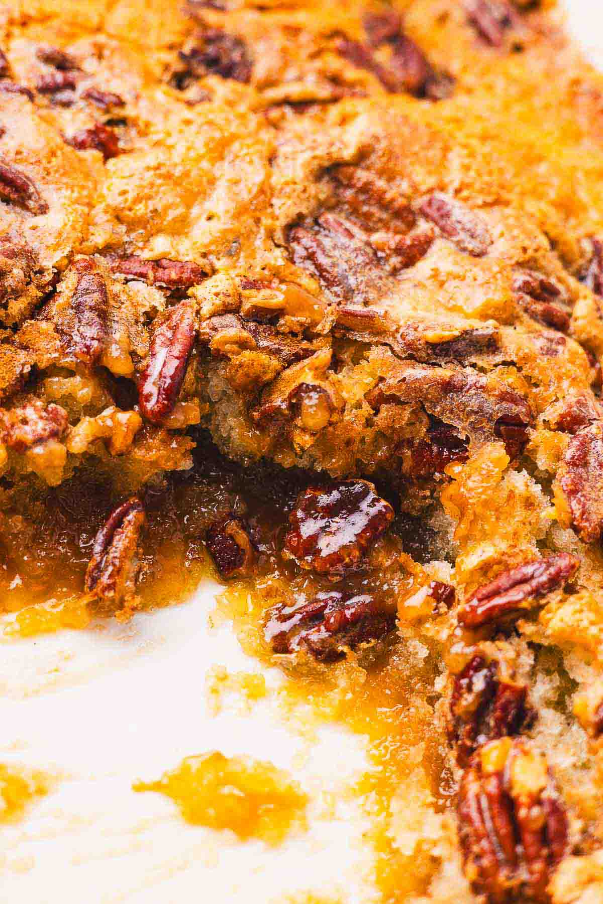 Pecan cobbler in a baking dish with a scoop taken out.