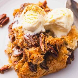 Pecan bread cobbler with ice cream and pecans on a plate.