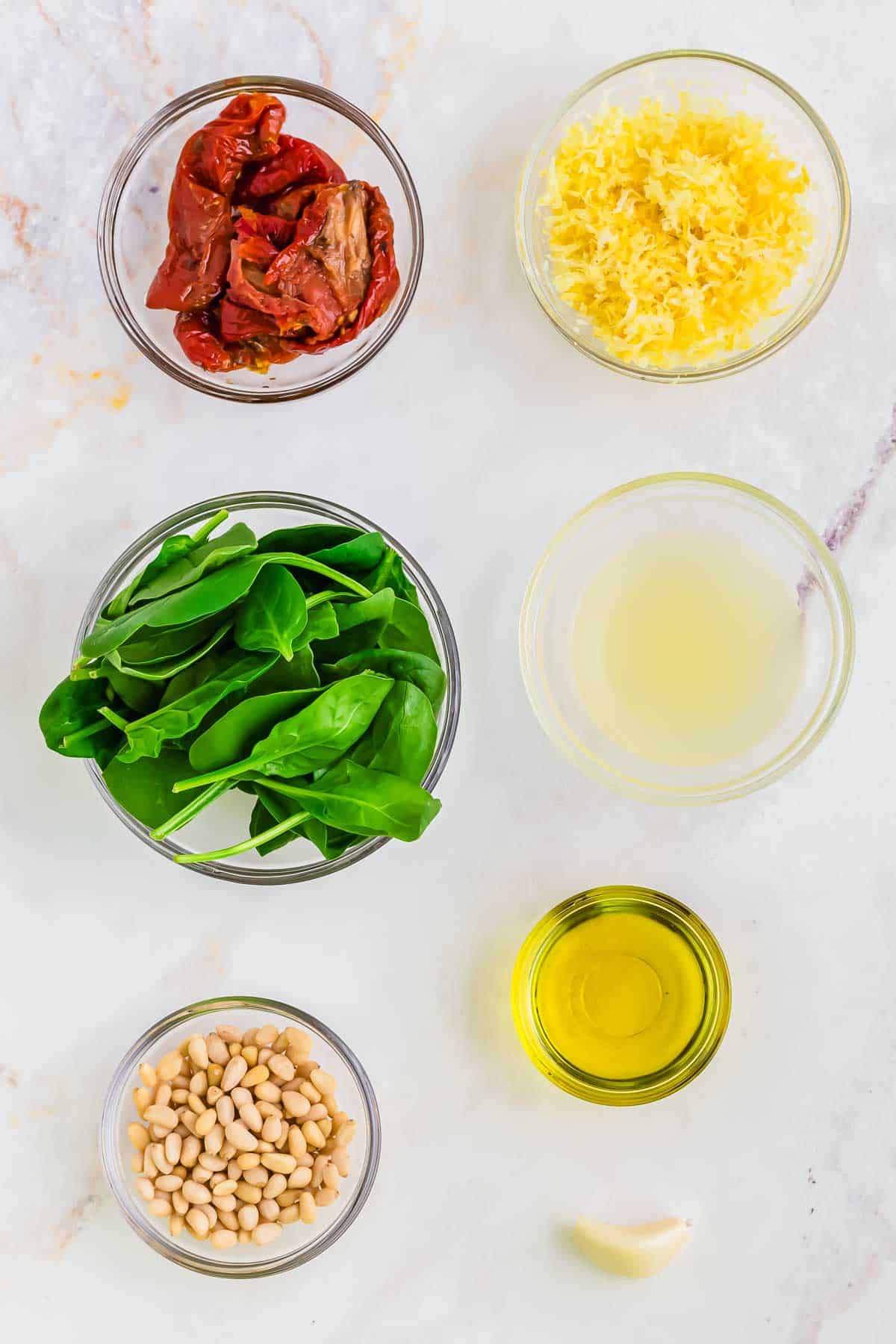 Ingredients to make pesto salmon recipe in small bowls on marble surface.