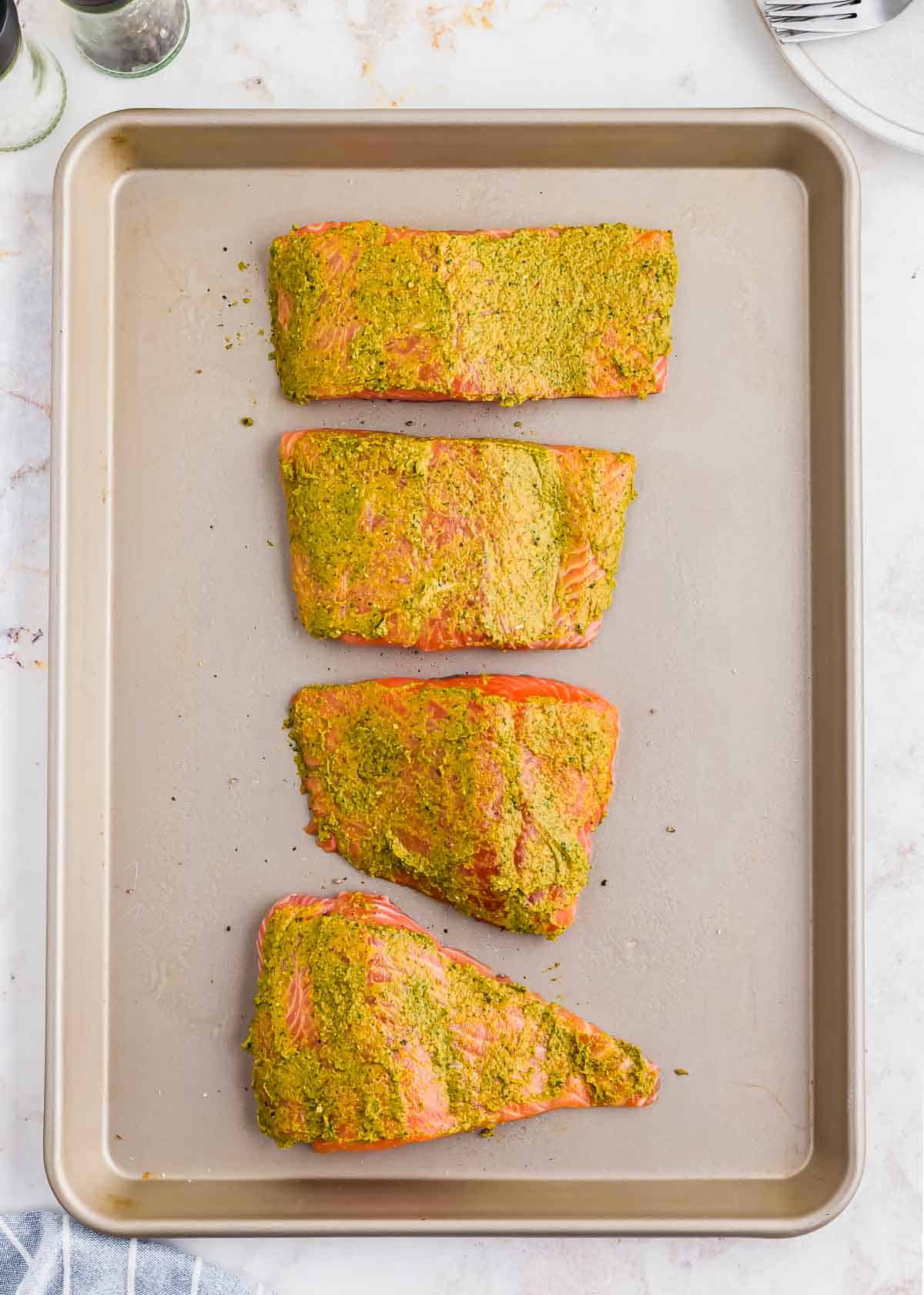Salmon filets on a baking sheet with pesto spread on top of each.