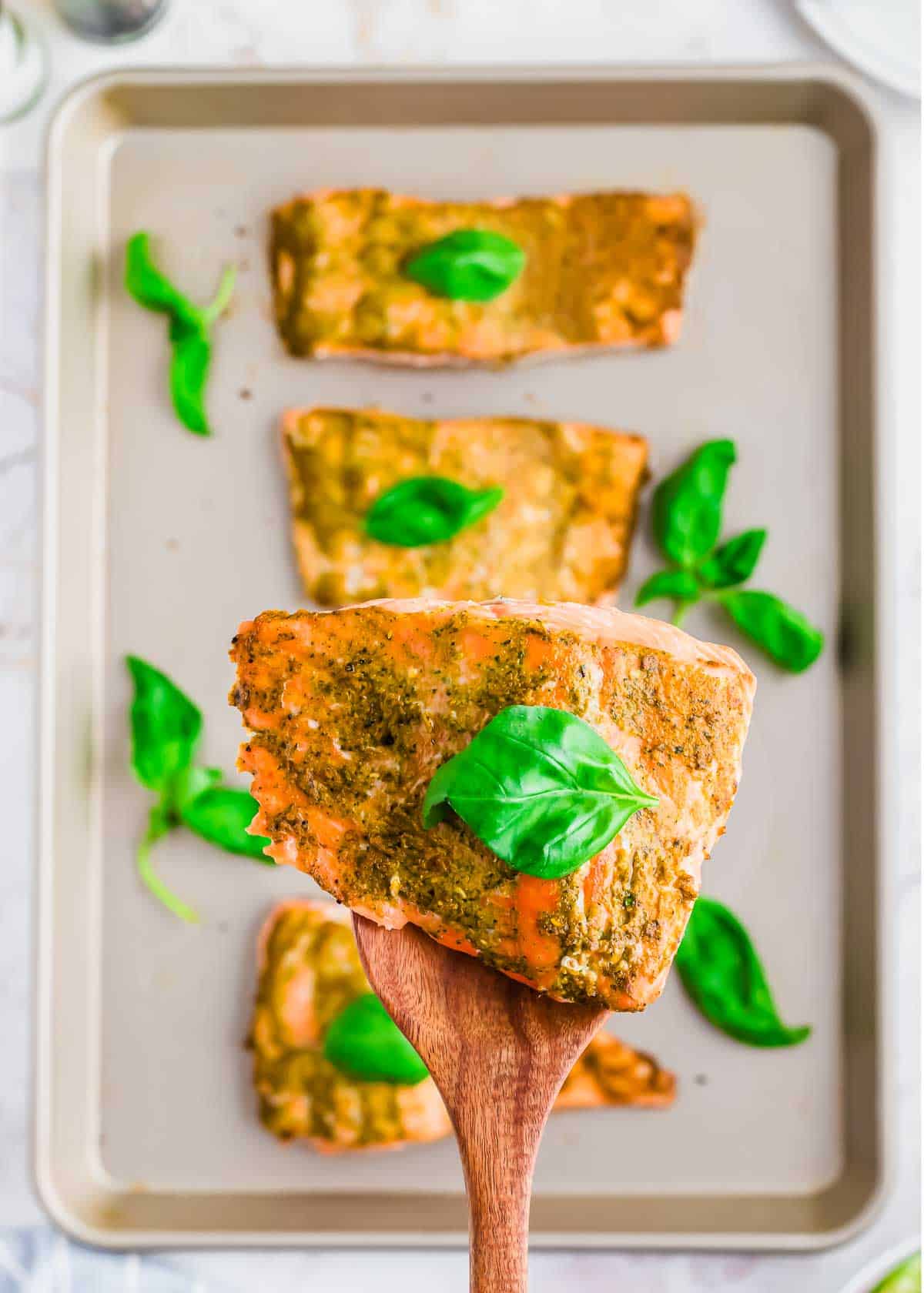 A wooden spoon with a filet of baked pesto salmon.