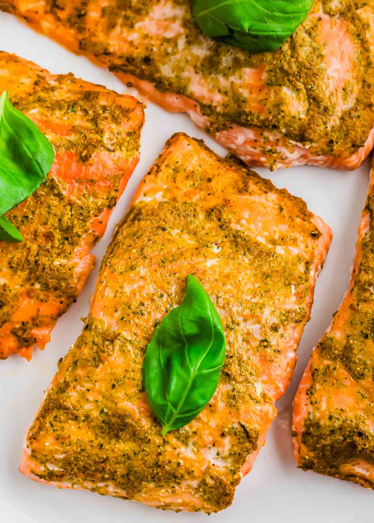 Pesto salmon filets garnished with basil on a white plate.