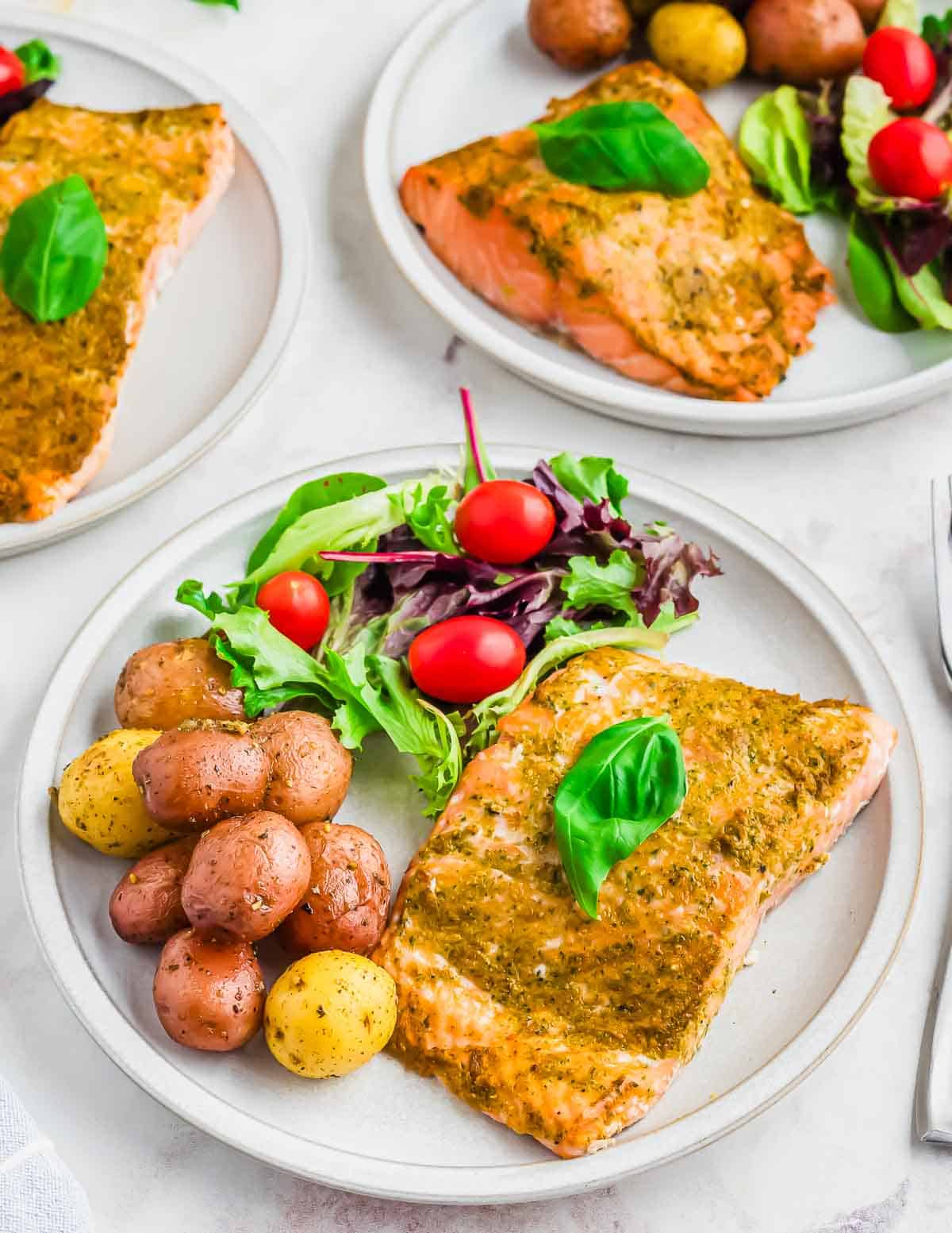 Pesto salmon on a plate with roasted potatoes and salad.