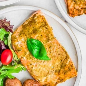 Oven baked pesto salmon on a plate with fresh basil leaves.