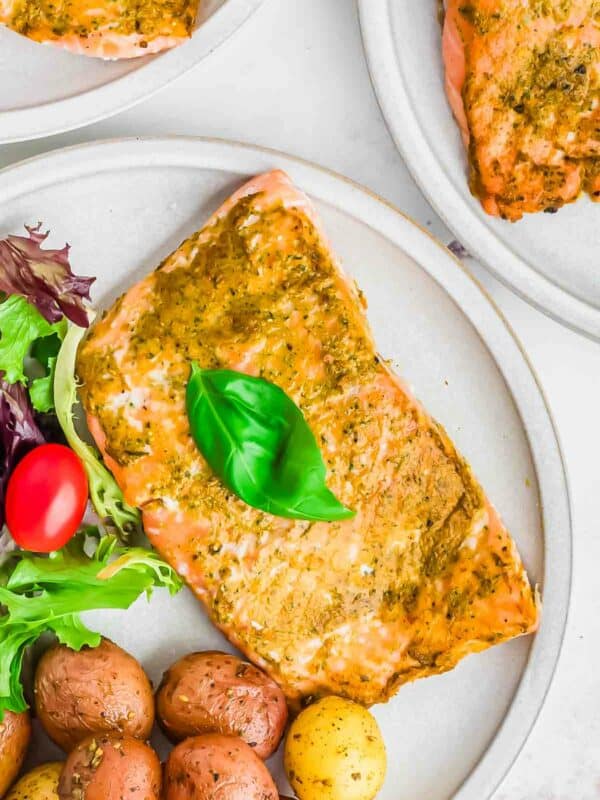 Oven baked pesto salmon on a plate with fresh basil leaves.