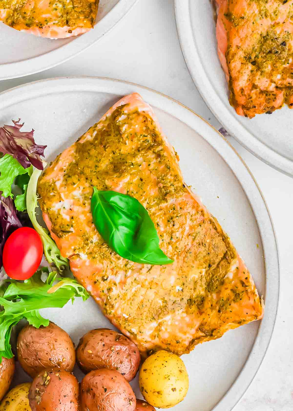 Oven baked pesto salmon on a plate with fresh basil leaves.