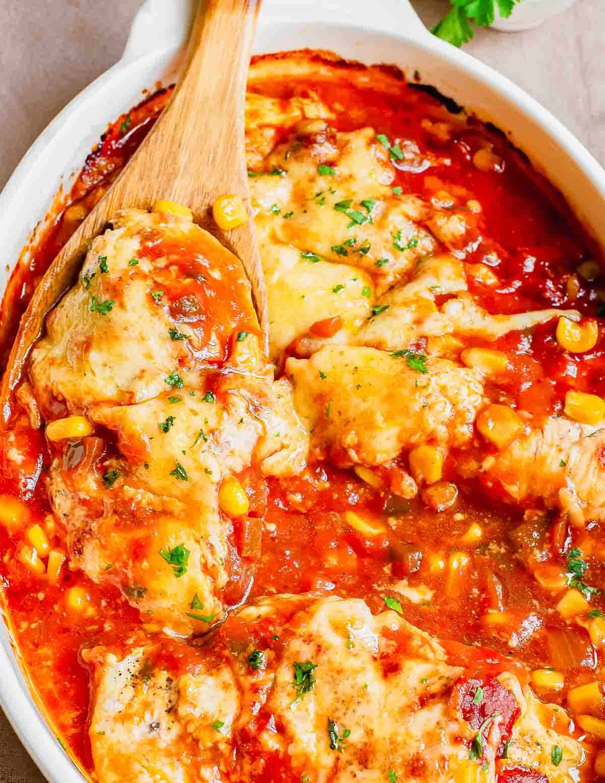 Salsa chicken in a baking dish with a wooden spoon.