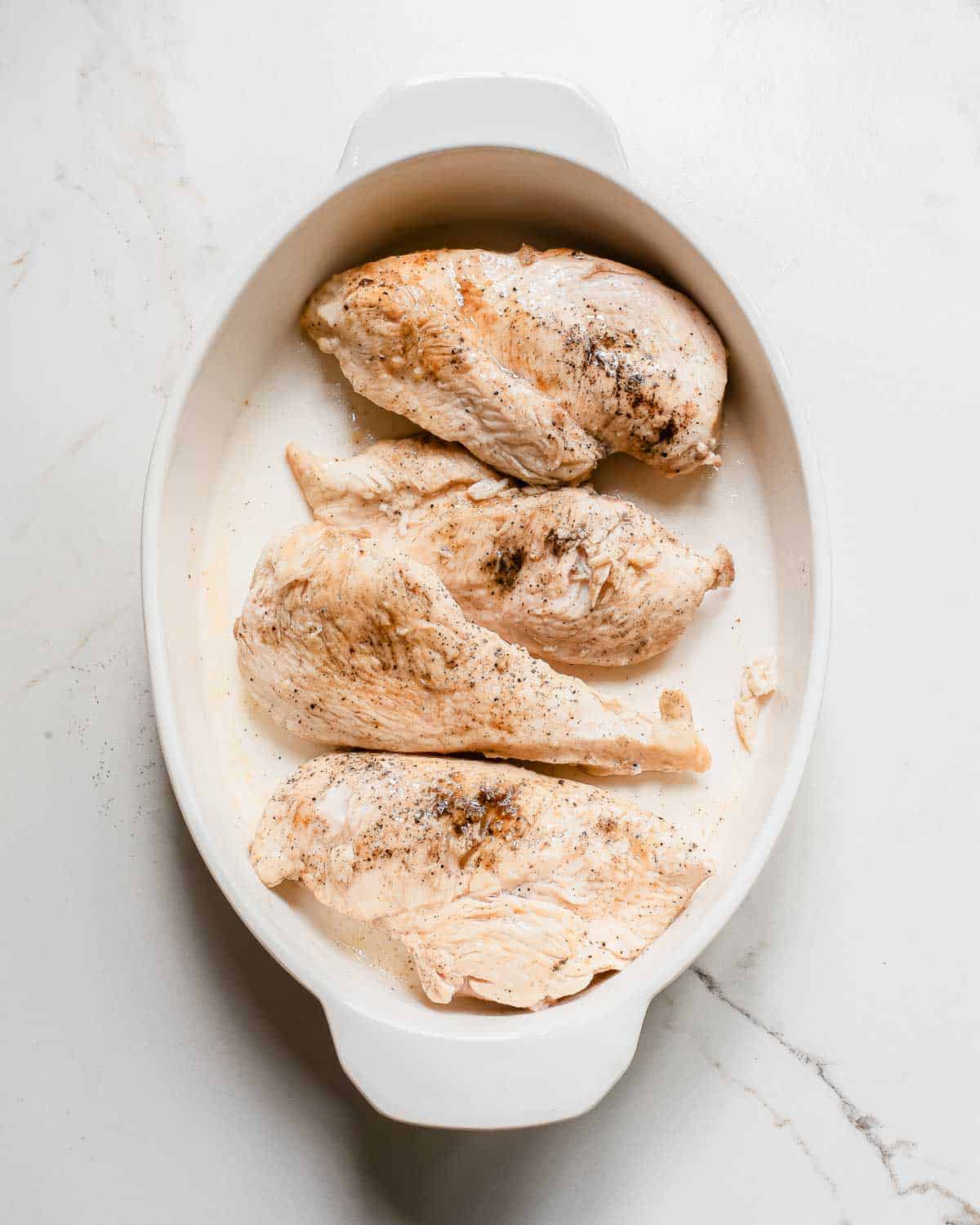 Seared chicken breasts in a white dish on a marble countertop.