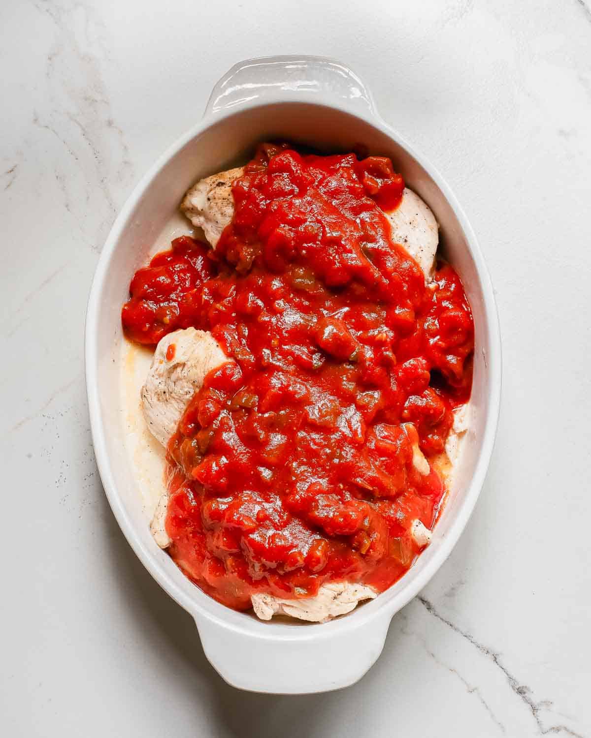 A white casserole dish with chicken breasts and salsa on top.