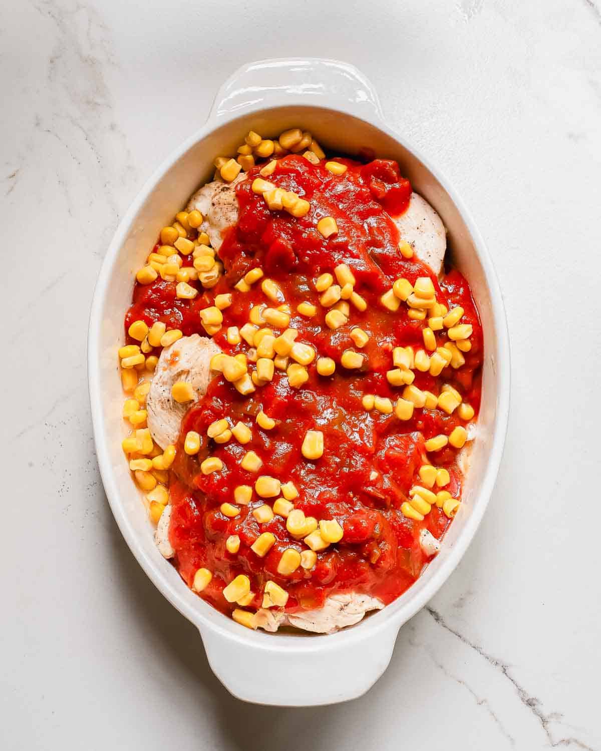 A white baking dish with chicken, salsa and corn in it.