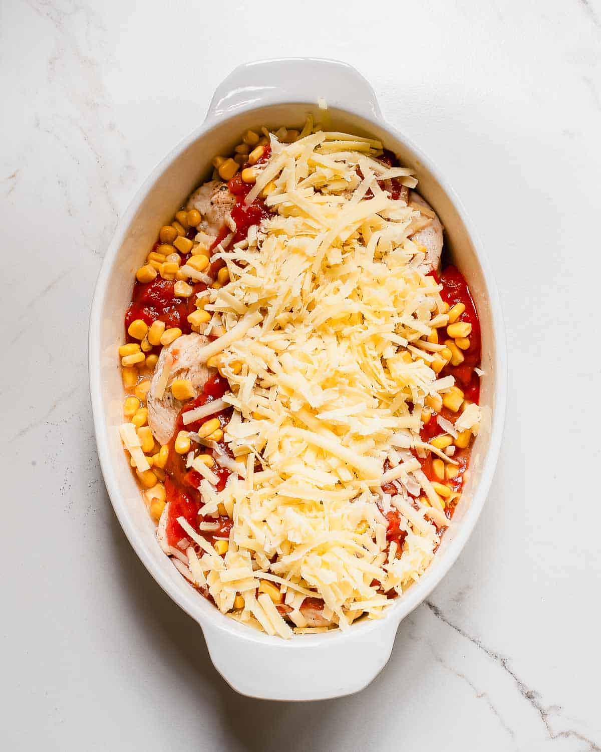 A white dish filled with chicken, corn, salsa and cheese.