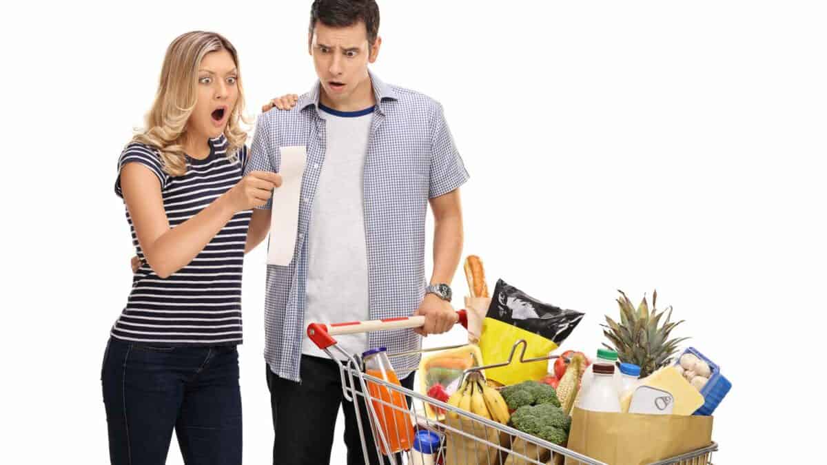 A man and woman standing next to a shopping cart full of groceries.