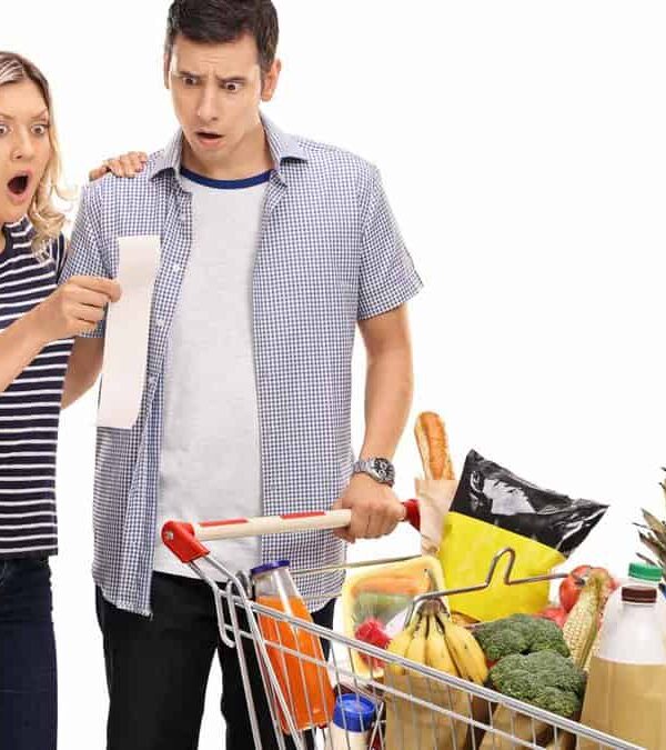 A man and woman standing next to a shopping cart full of groceries.