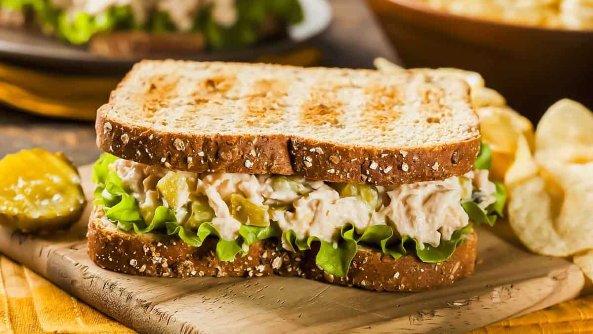 A sandwich with tuna salad and chips on a wooden cutting board.