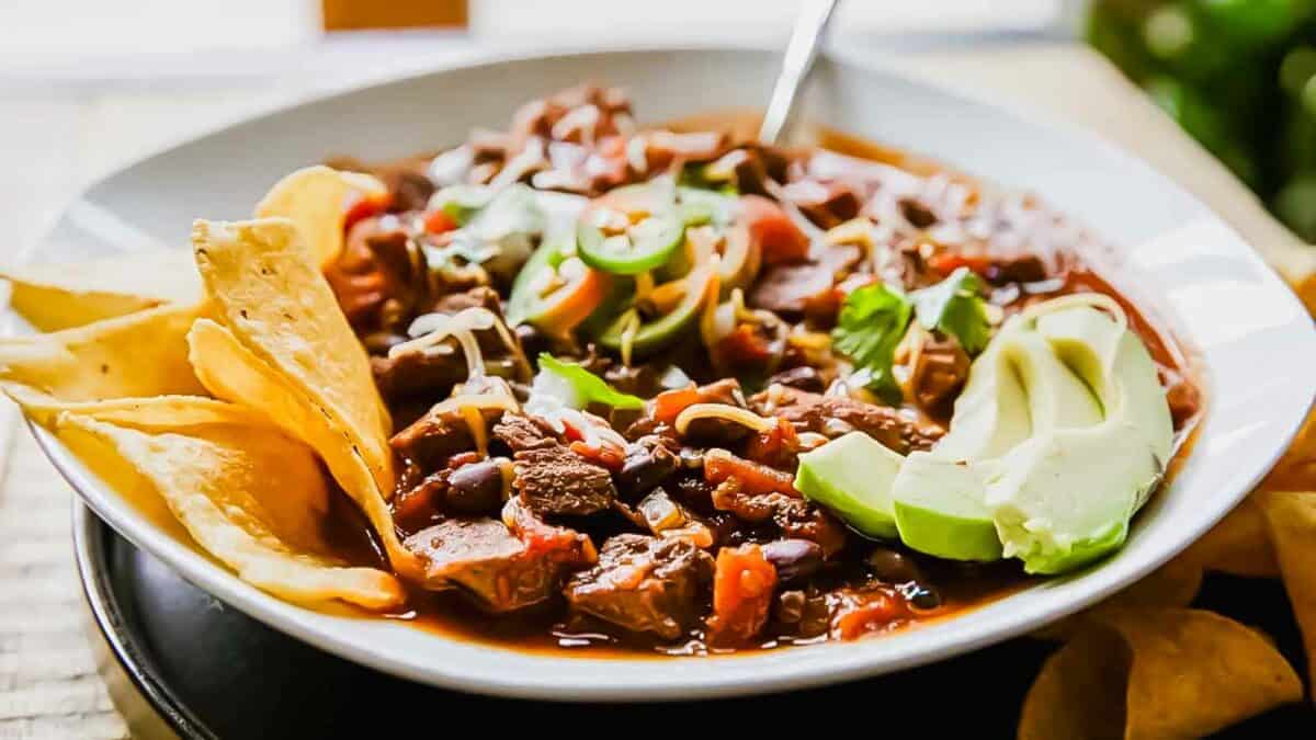 A bowl of chili with tortilla chips and guacamole.