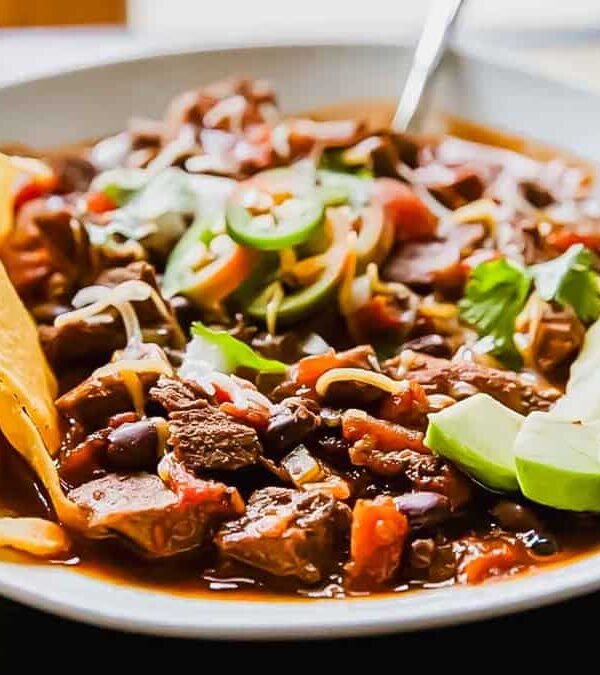 A bowl of chili with tortilla chips and guacamole.