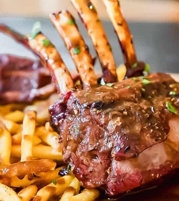 A steak with fries and sauce on a wooden cutting board.