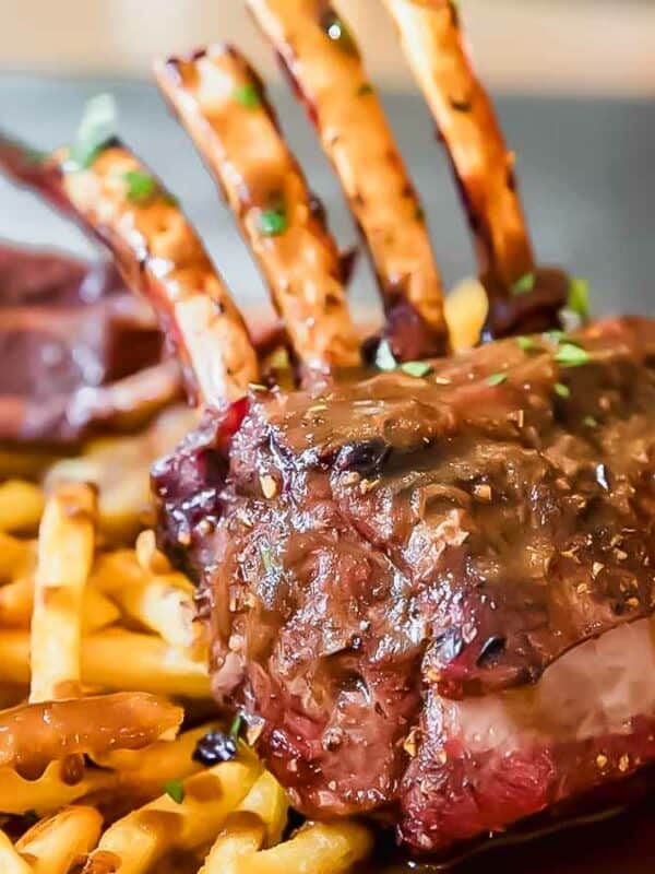 A steak with fries and sauce on a wooden cutting board.