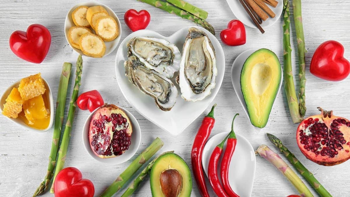 A variety of healthy aphrodisiac foods including oysters, fruits, vegetables, and honey on a wooden surface.