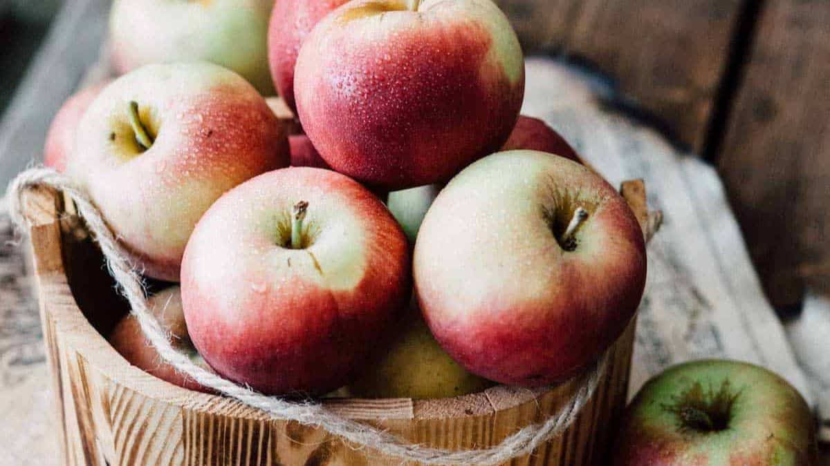 A basket of fresh, ripe apples on a wooden surface.