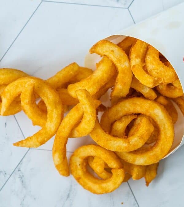 Curly fries spilled from a fast-food container onto a white surface.