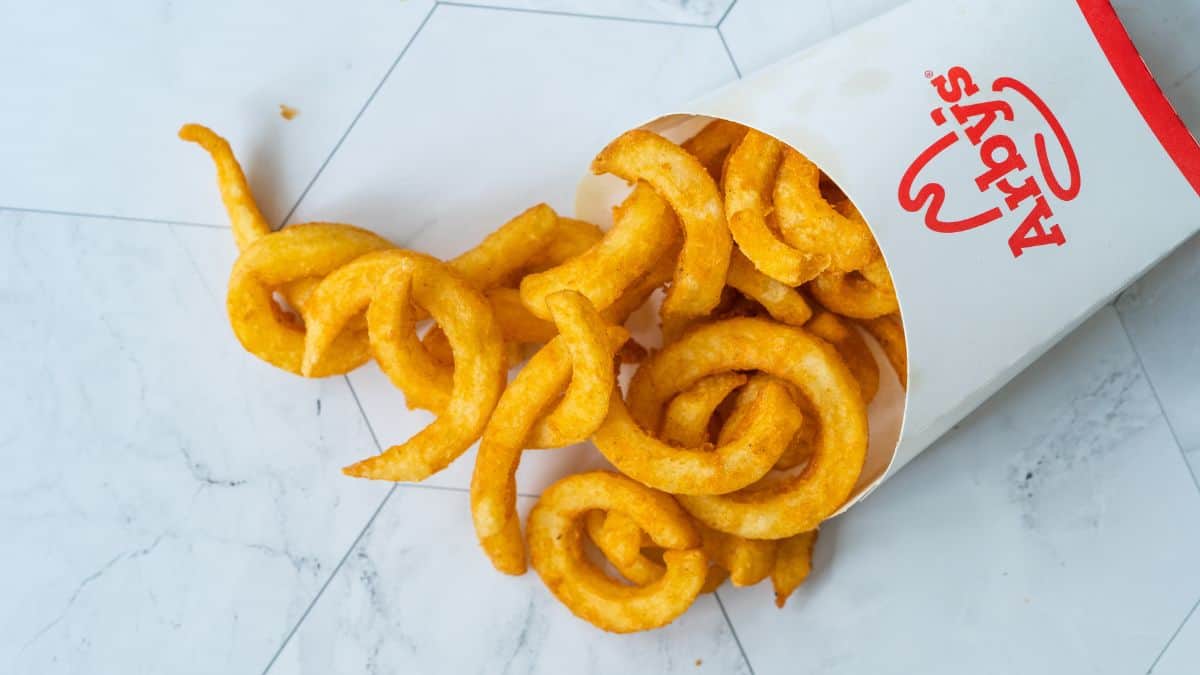 Curly fries spilled from a fast-food container onto a white surface.