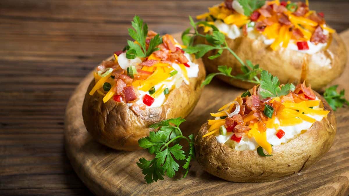 Three baked potatoes with cheese and bacon on a wooden board.