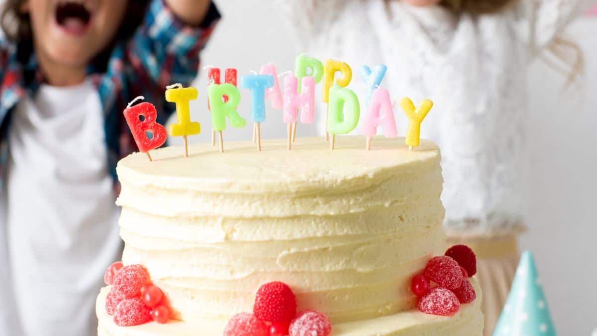 Two children are standing in front of a birthday cake.