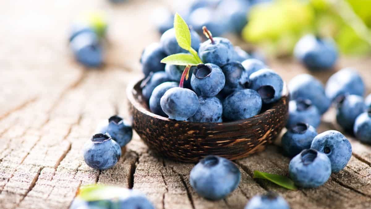 A bowl of fresh blueberries on a wooden surface.