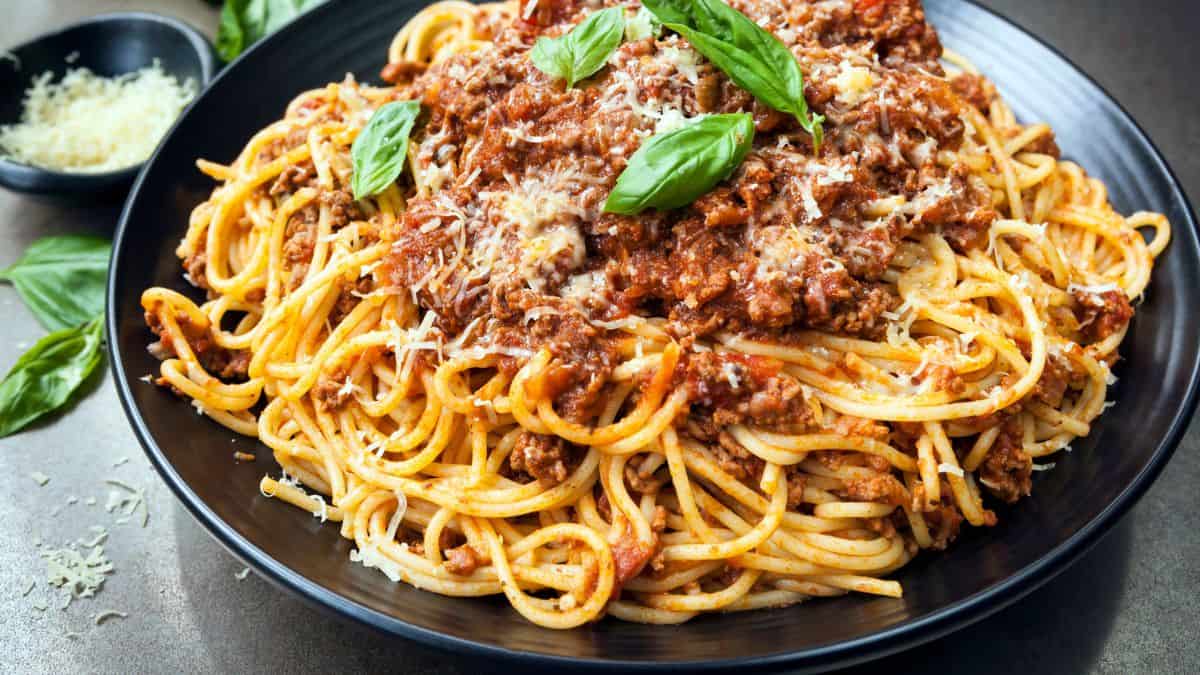 A plate of spaghetti with meat sauce and basil garnish.