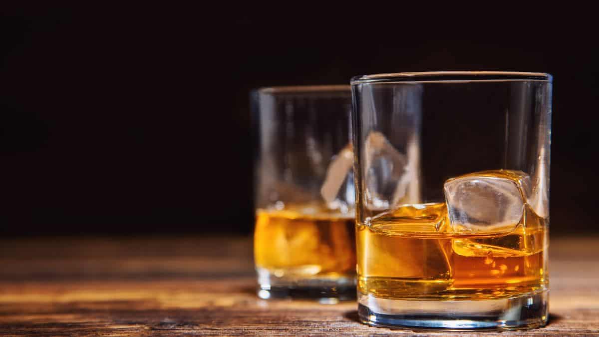Two glasses of whiskey with ice cubes on a wooden table.