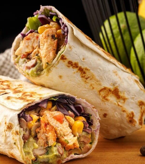 Chicken wrap with fresh vegetables and avocado on a wooden table.