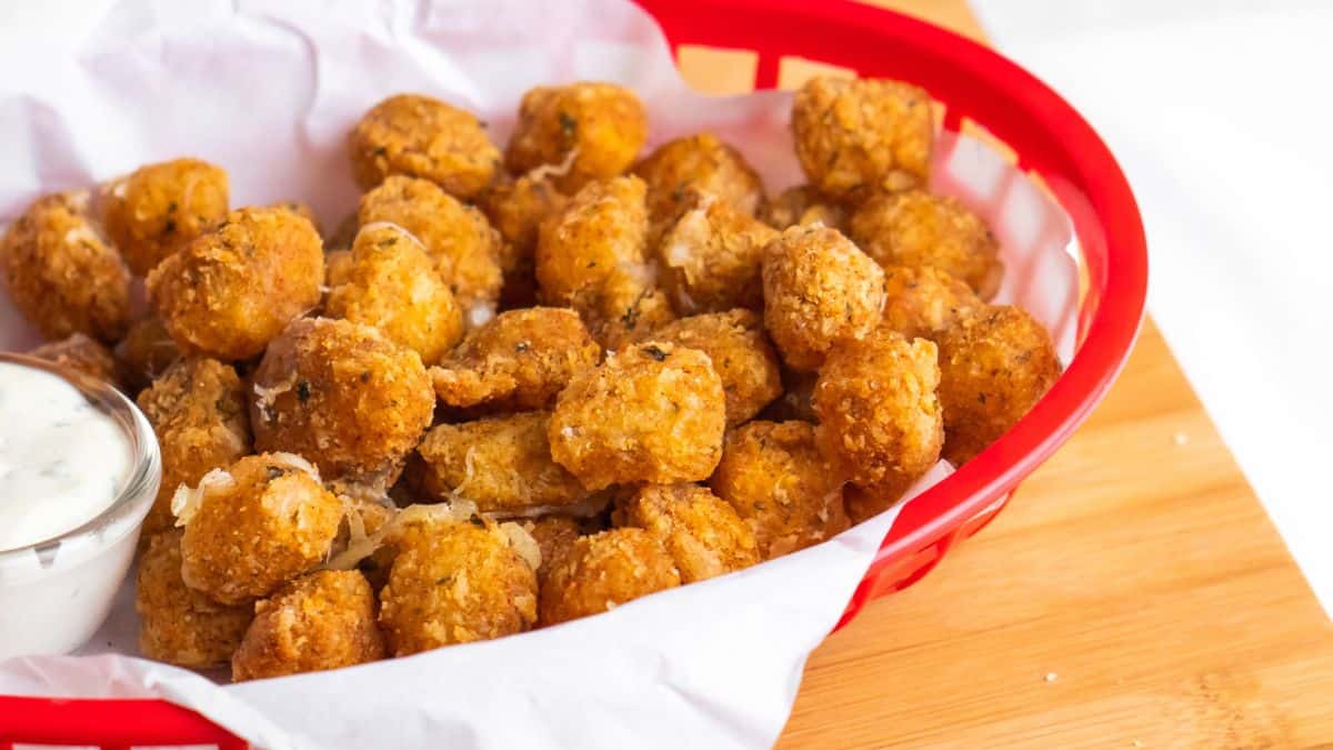 A basket full of tater tots with dipping sauce.