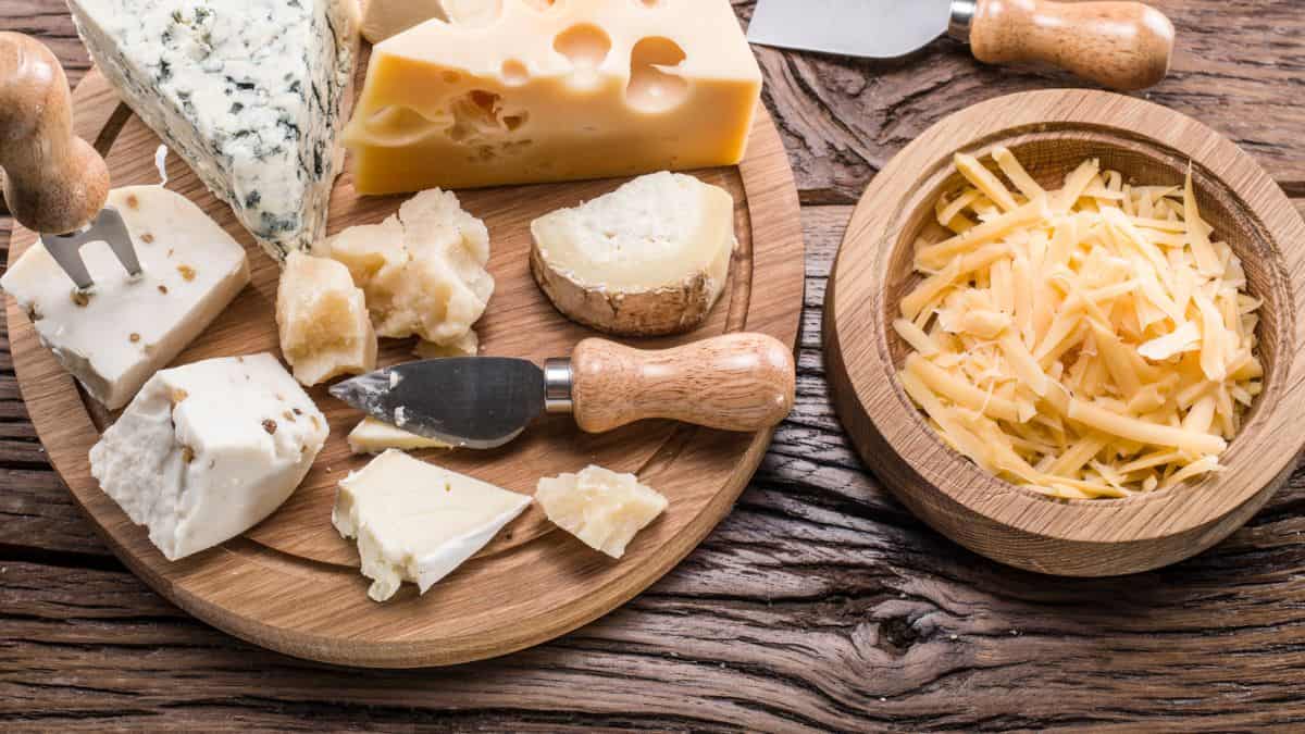 Various types of cheese on a wooden cutting board.