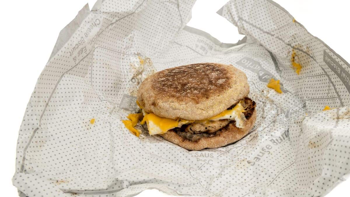 Partially unwrapped breakfast sandwich with egg, cheese, and sausage on a white background.