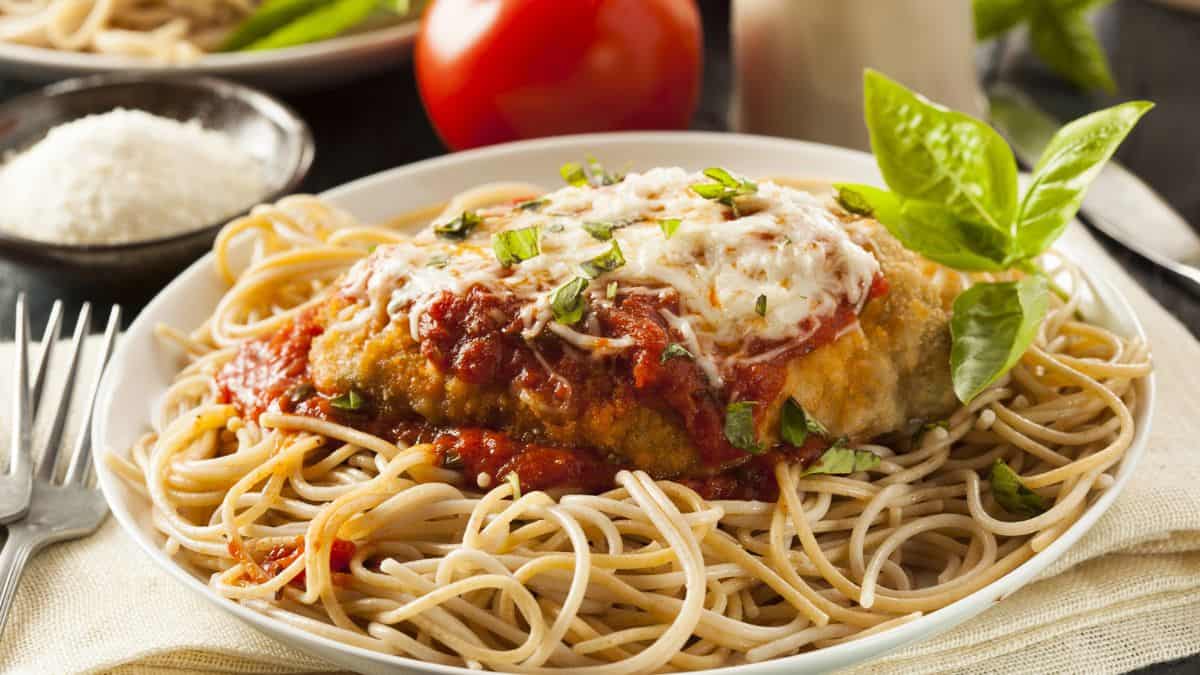 A plate of spaghetti topped with a breaded chicken cutlet, marinara sauce, melted cheese, and a sprig of basil.