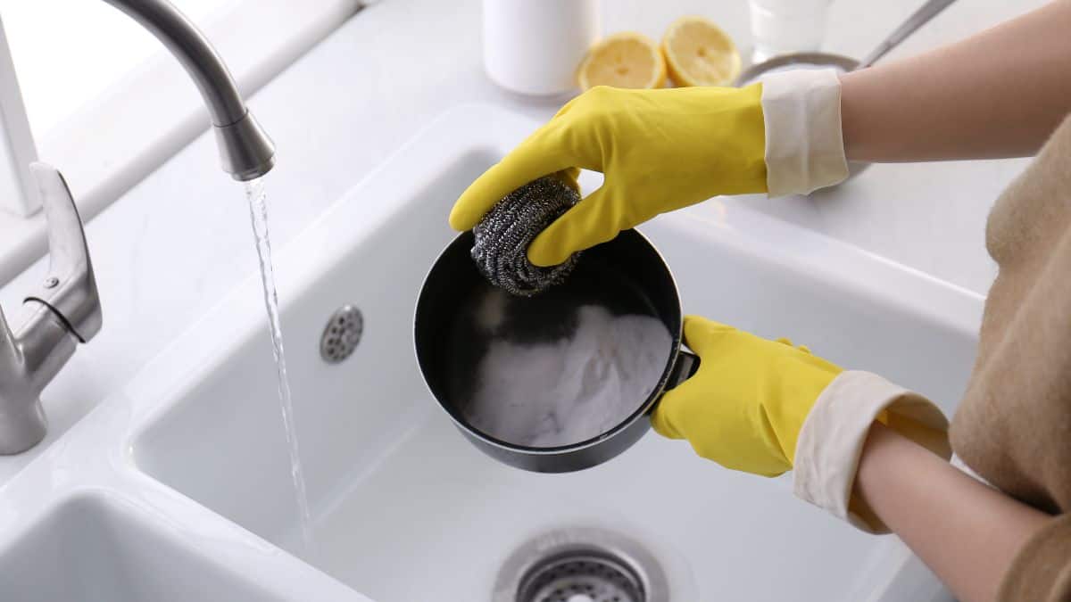 A woman wearing yellow gloves cleaning a sink.